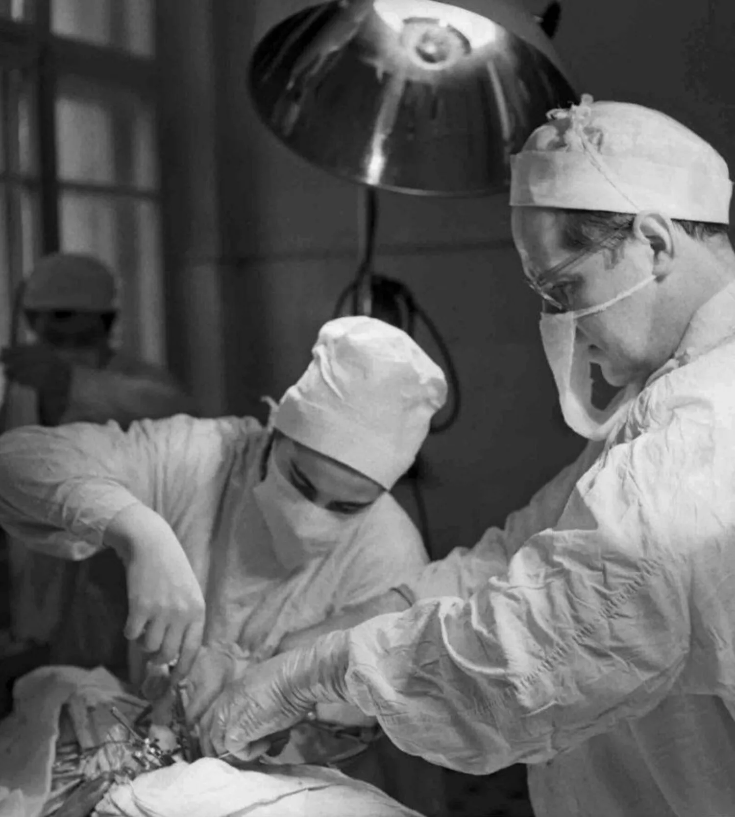 A surgical team in gowns and masks bent over an opened chest under operating lights, 1968.